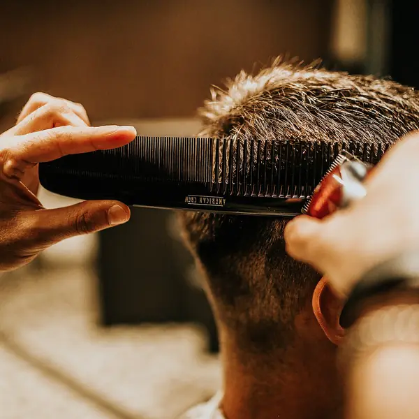 Barbeiro aparando o cabelo de um cliente com pente e máquina